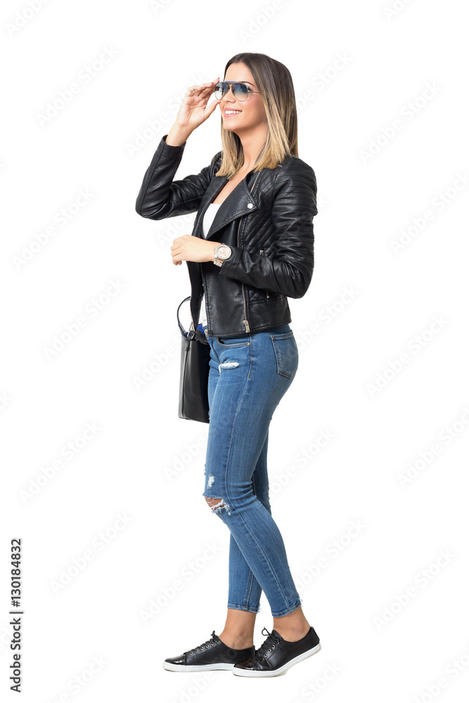Side view of young happy stylish woman in jeans touching sunglasses looking away. Full body length standing portrait isolated over white background. Side view of young happy stylish woman in jeans touching sunglasses looking away. Full body length standing portrait isolated over white background.