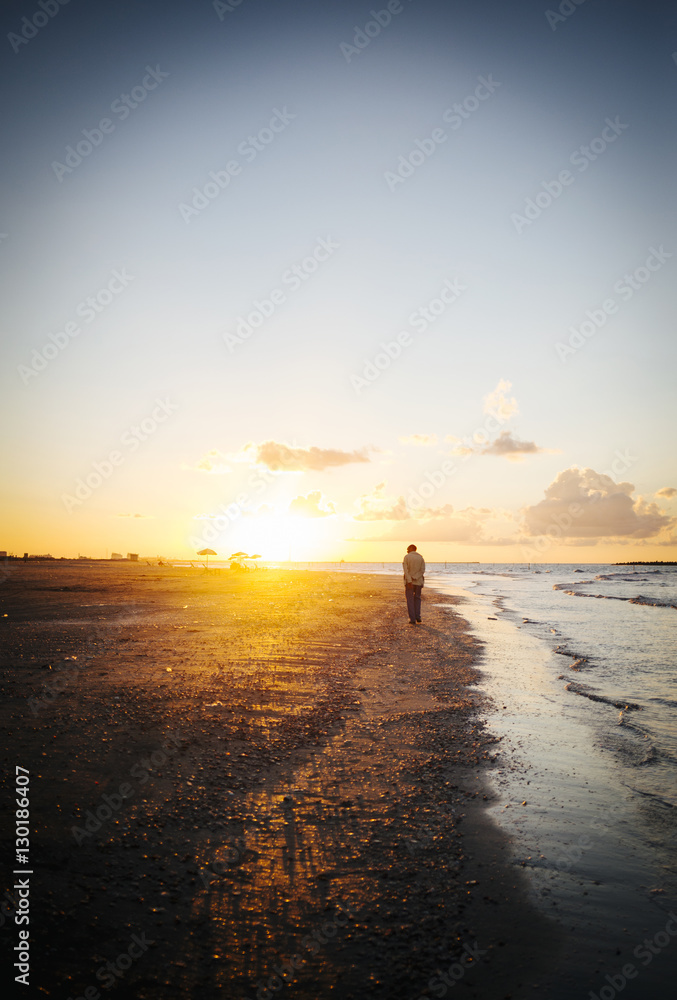 lonely man walking on the beach at sunset.