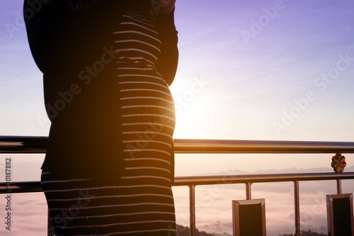 Pregnant woman standing with mountain view and foggy background.