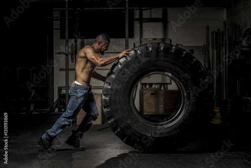Muscle Man in Jeans Pushing Large Tire