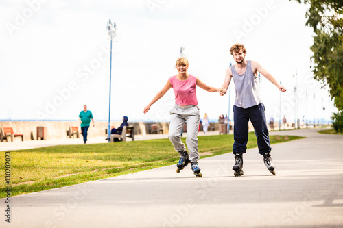 Young couple rollerblading in park holding hands.