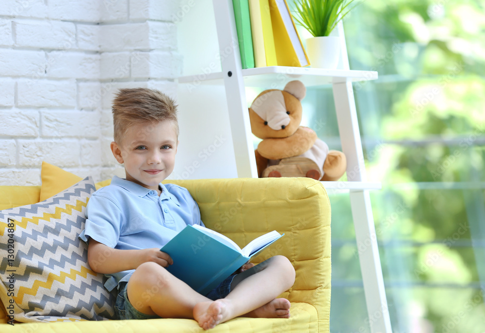 Little boy sitting on sofa and reading book