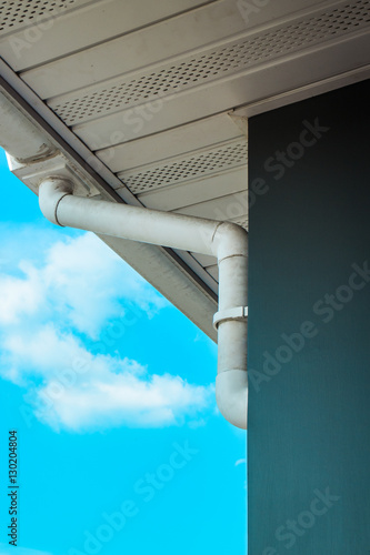 New white rain gutter. Drainage System with Plastic Siding Soffits and Eaves against blue sky