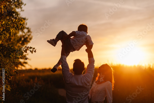 happy family playing with a baby in the park at sunset