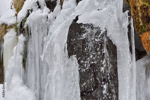 Ice icicles hang on mountain rocks in a cold winter day with water-drops from a small waterfall