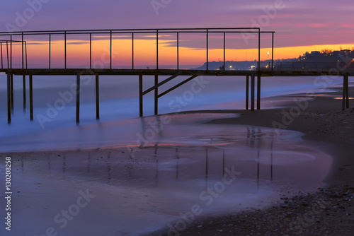 old pier, sunset on the beach, the city lights in the distance on the beach. Beautiful sea sunset.   © Ann Stryzhekin