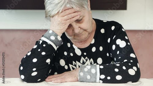 old woman shakes her head in disbelief sitting in her kitchen photo