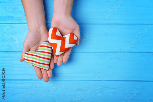 Female hands holding handmade hearts on blue wooden background