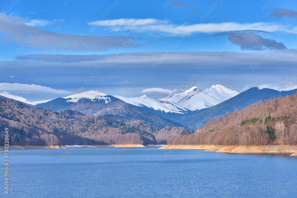 Mountain lake panorama against cloudy sky and mountains covered