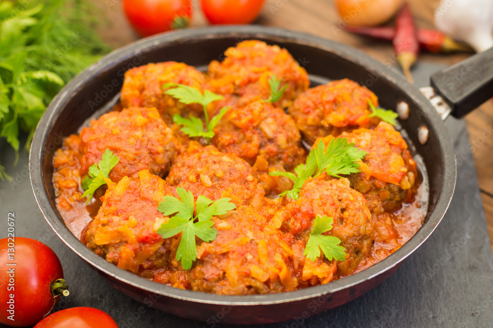 Meatballs in sweet and sour tomato sauce in the pan. Wooden background. Close-up