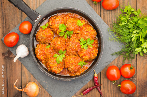 Meatballs in sweet and sour tomato sauce in the pan. Wooden background. Close-up