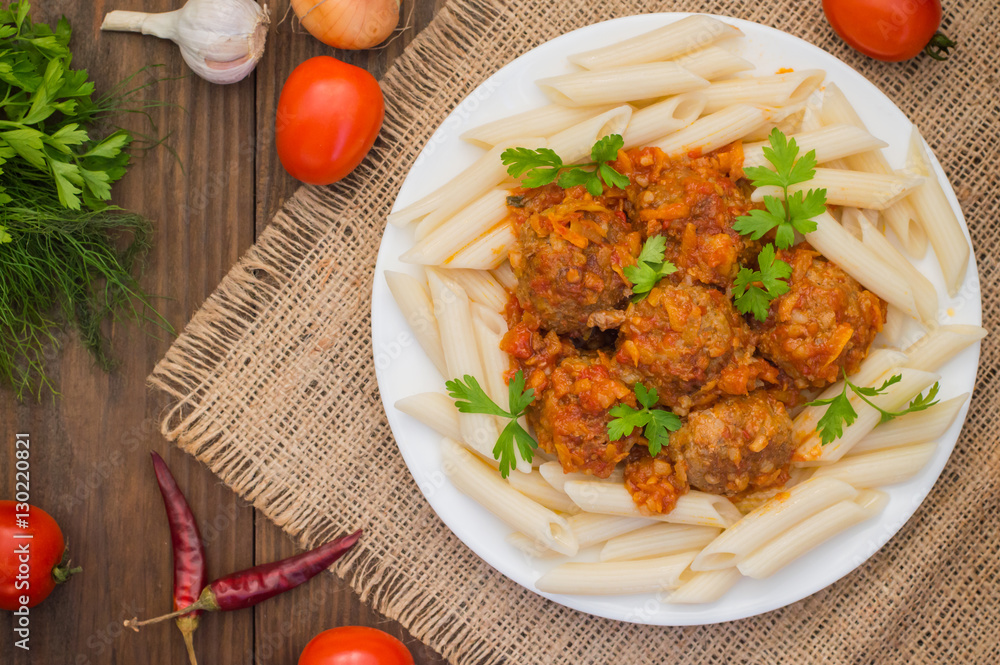 Meatballs with pasta penne in tomato sauce on a white plate. Wooden rustic background. Top view. Close-up Meatballs with pasta penne in tomato sauce on a white plate. Wooden rustic background. Top view. Close-up