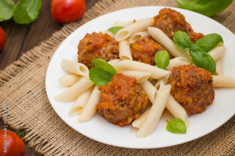 Meatballs with pasta penne in tomato sauce on a white plate. Wooden rustic background. Top view. Close-up Meatballs with pasta penne in tomato sauce on a white plate. Wooden rustic background. Top view. Close-up