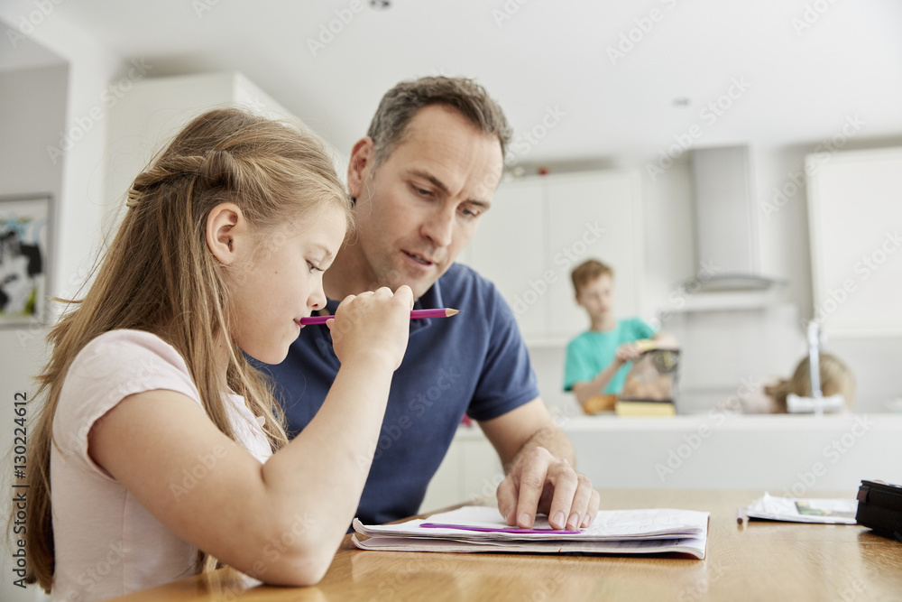 A young girl and her father sitting looking at her school books, doing her homework. A young girl and her father sitting looking at her school books, doing her homework.