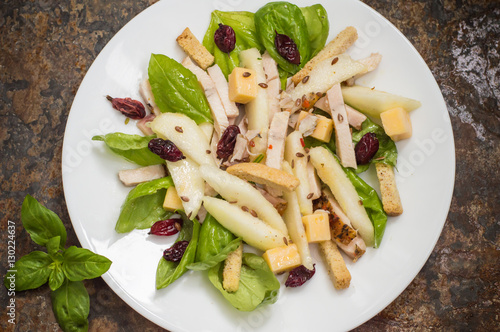 Chicken salad, pears, dried gooseberries and currants, cheese on basil leaves. Wooden background. Top view. Close-up