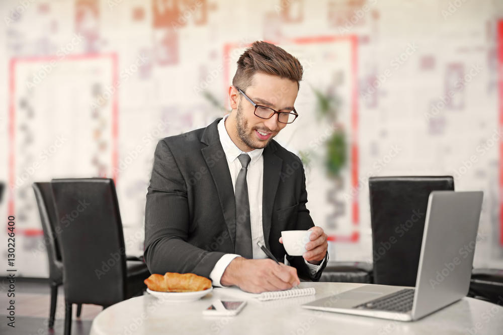Young businessman working in cafe while having snack Young businessman working in cafe while having snack