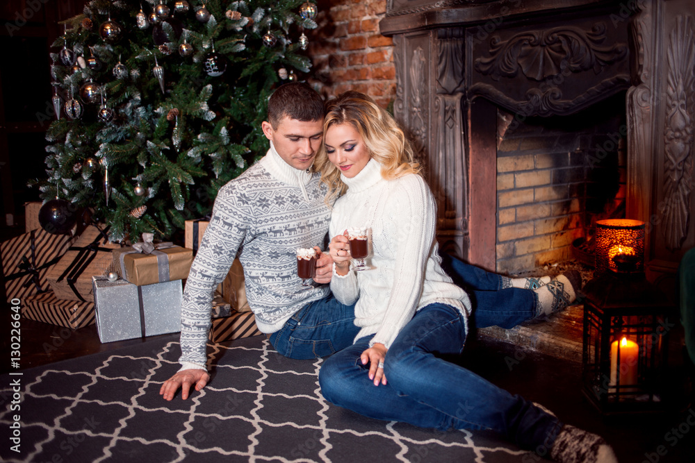 Merry Christmas. Young couple celebrating New Year at home. Man and a woman by the fireplace Merry Christmas. Young couple celebrating New Year at home. Man and a woman by the fireplace