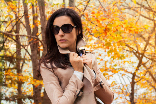 Fall Concept - beautiful autumn woman wearing trench coat and sunglasses standing in nature