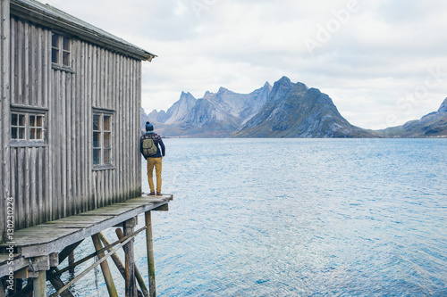 A man with a backpack standing on a wooden pier. Pier in the sea of the Gulf, around the Bay of high rocky mountains. Traveler, traveling, nature. Copy space.