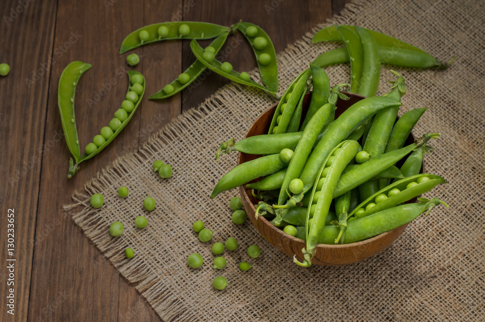Pea pods in a wooden bowl on sacking. background. Top view. Close-up Pea pods in a wooden bowl on sacking. background. Top view. Close-up