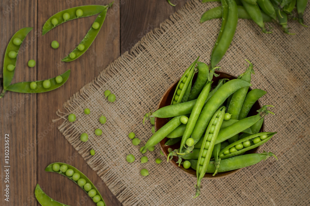 Pea pods in a wooden bowl on sacking. background. Top view. Close-up Pea pods in a wooden bowl on sacking. background. Top view. Close-up