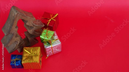 Tilt up to  a wooden Christmas treewith colourful gifts which are remove by human hands and copy space on an infinite red backdrop and back photo