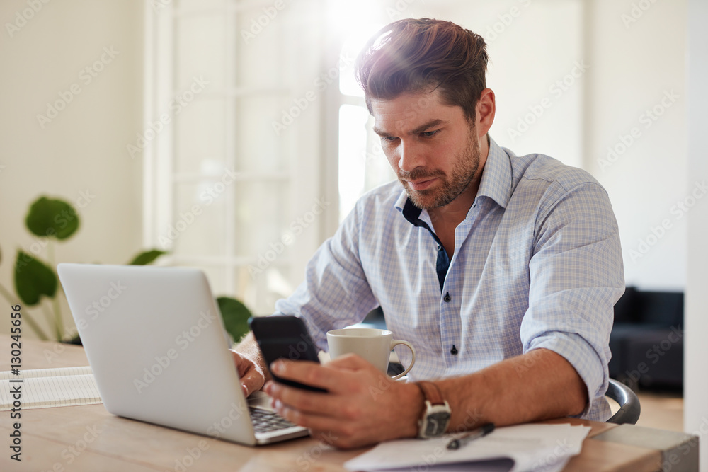 Young man working with laptop and mobile phone at his home offic
