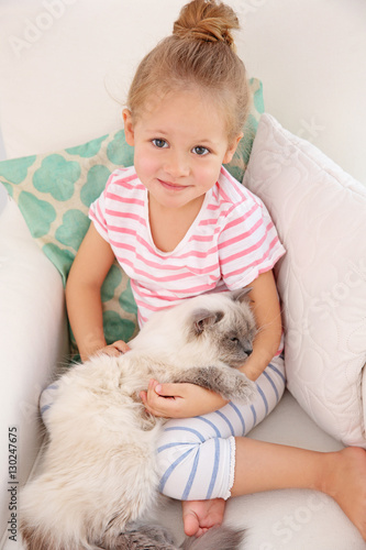 Cute little girl sitting in armchair with fluffy cat