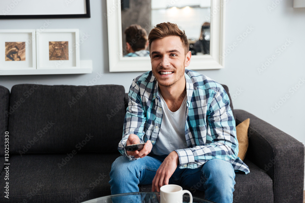 Fototapeta premium Joyful young bristle man holding remote control while watching TV.