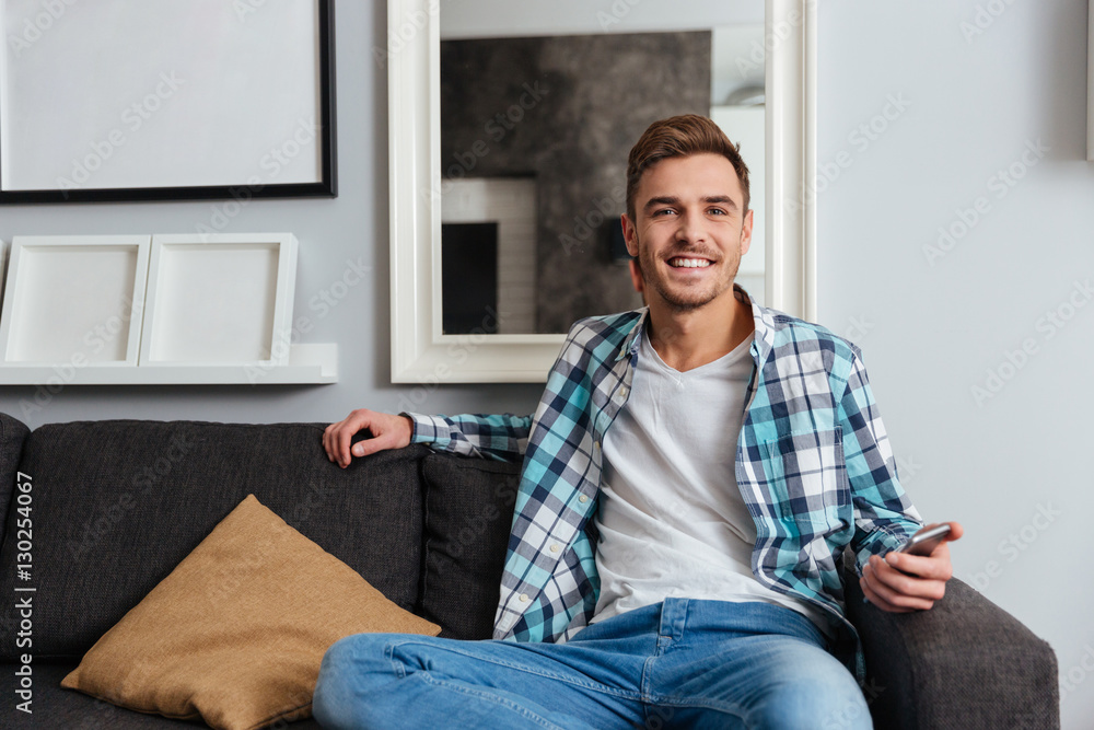 Young smiling man sitting on sofa in home while chatting
