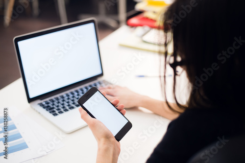 Woman's hands using mobile phone and laptop at the office