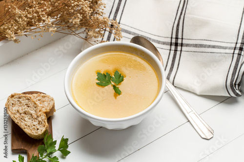 Sopa en un cuenco blanco junto a rodajas de pan, una cuchara y una servilleta sobre una mesa blanca. Vista superior y de cerca photo