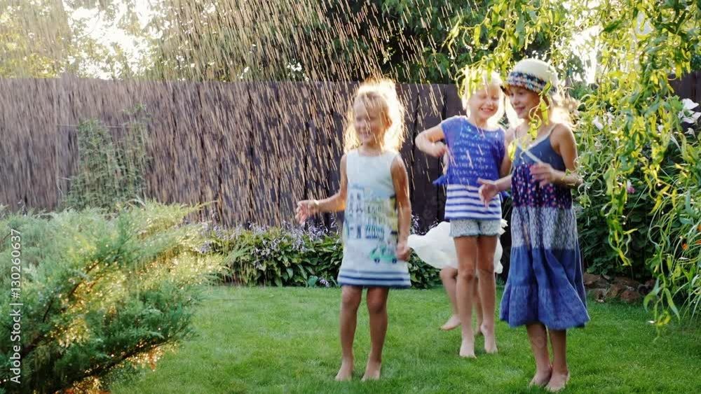 Four carefree cheerful children laughing in the garden under a spray of water. Concept - friendship and childhood Four carefree cheerful children laughing in the garden under a spray of water. Concept - friendship and childhood