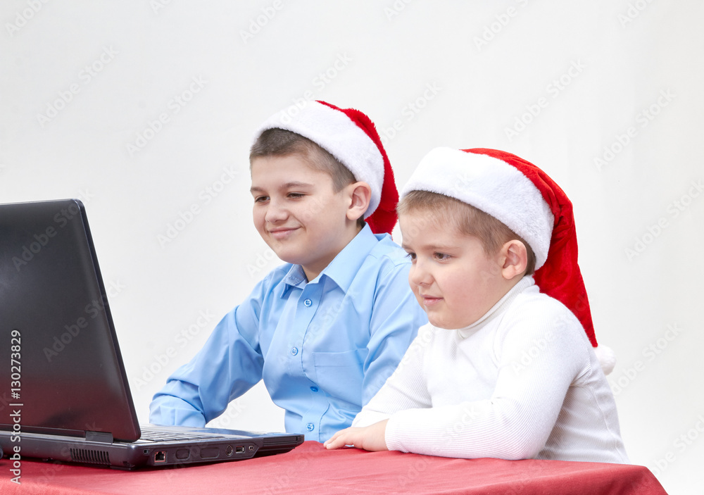 Children in santa hat look interesting programs on the laptop screen Children in santa hat look interesting programs on the laptop screen