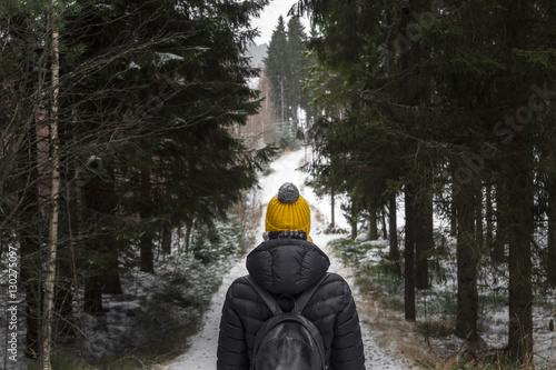 Canvas Print alone young woman in black down jacket and yellow knitted hat with rucksack on t