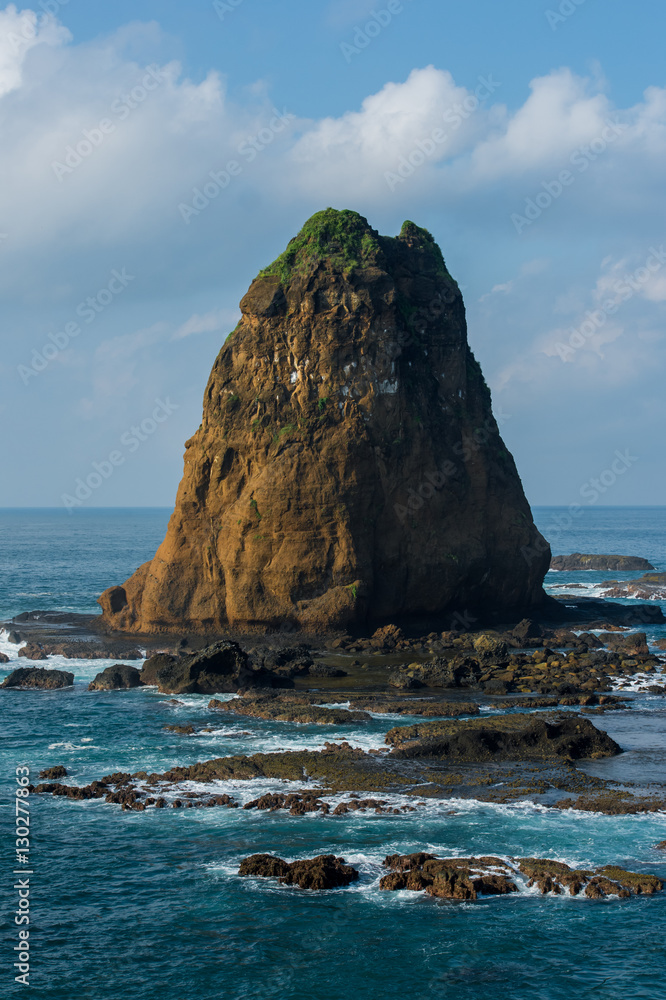 A large boulder stands on reefs among small waves (Indonesia)