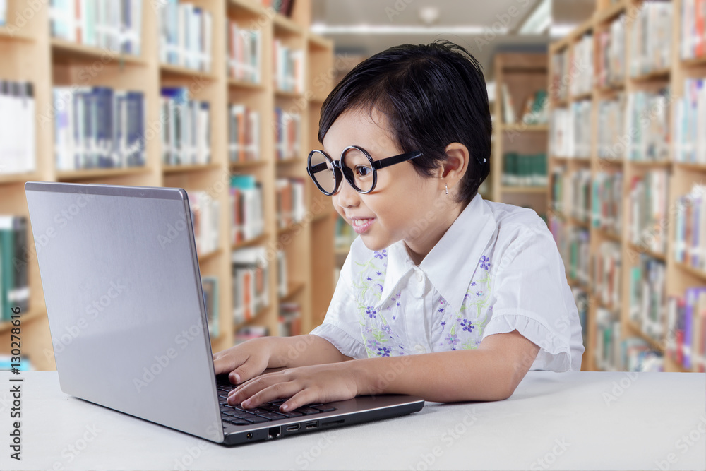 Clever girl using laptop on desk in library Clever girl using laptop on desk in library