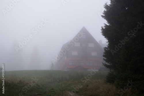 Challet in misty woods with thick fog and trees silhouettes. Slovakia