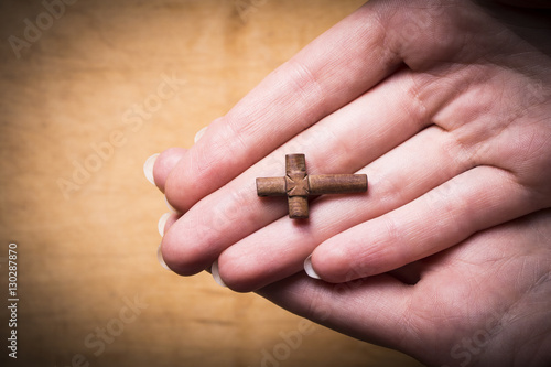 Cross in female hands on a wooden background. 