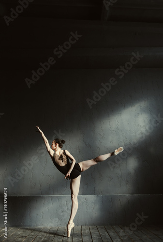 Elegant ballet dancer stretching in the dark lighted room