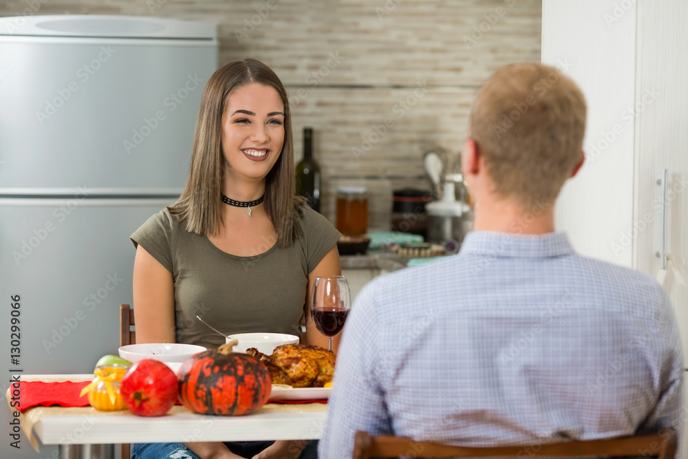 Young couple is sitting at the dining table and having a Thanksgiving dinner at home. Rear view of young man talking with his beautiful young wife. Young couple is sitting at the dining table and having a Thanksgiving dinner at home. Rear view of young man talking with his beautiful young wife.