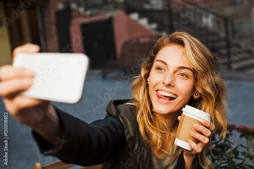 Young beautiful woman makes selfie with coffee on cafe terrace