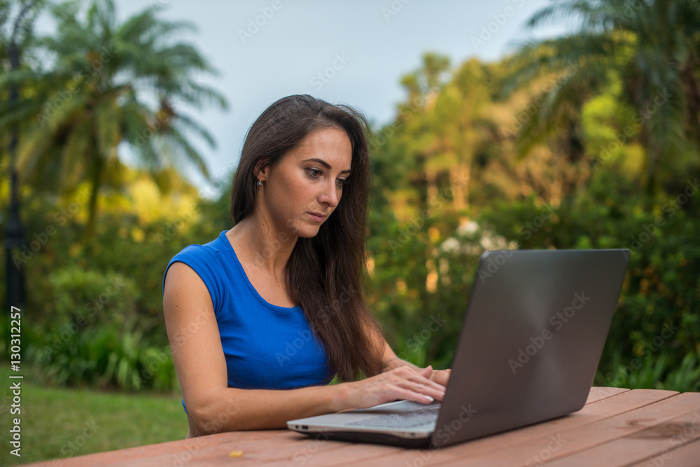 Young female freelancer working at project on her laptop in tropical park Young female freelancer working at project on her laptop in tropical park