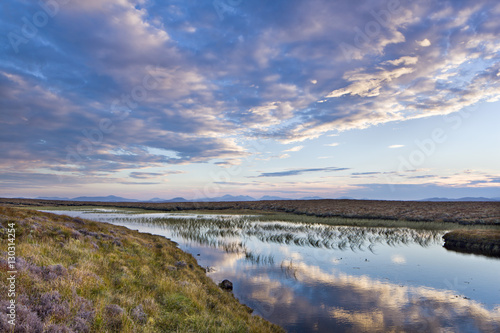 Evening reflections in a lochan on the peaty moreland of Lewis, with the mountains of Harris in the distance, Isle of Lewis, Outer Hebrides, Scotland photo