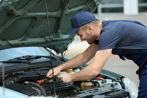 Mechanic standing in front of the open hood and repairing the car