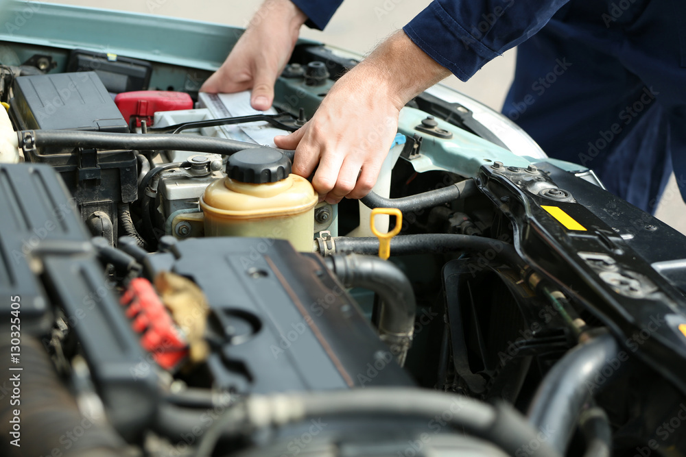 Mechanic hands checking up of serviceability of the car in open hood, close up Mechanic hands checking up of serviceability of the car in open hood, close up