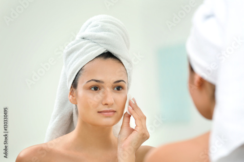 Beautiful girl cleaning face with sponge in front of mirror