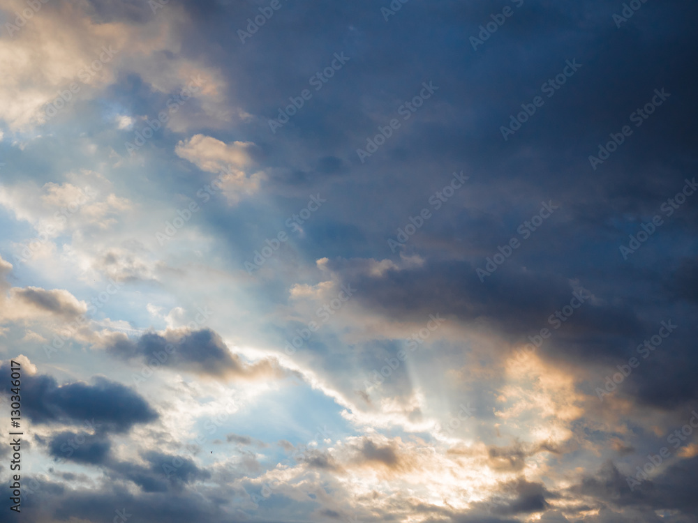 Obraz premium Picture of the sunset cloudy sky reflecting orange sun rays. Background of the still blue sunset sky with sun rays reflecting from the clouds.