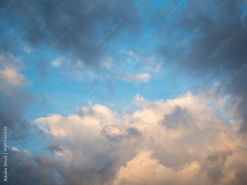Picture of the sunset cloudy sky reflecting orange sun rays. Background of the still blue sunset sky with sun rays reflecting from the clouds.