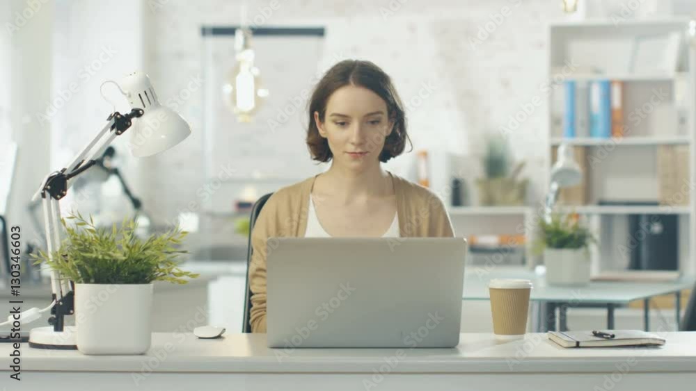 Portrait Shot of a Creative Woman Sitting at Her Desk. Using Notebook. She Sits in a Light and Modern Office. Shot on RED Cinema Camera in 4K (UHD). Portrait Shot of a Creative Woman Sitting at Her Desk. Using Notebook. She Sits in a Light and Modern Office. Shot on RED Cinema Camera in 4K (UHD).